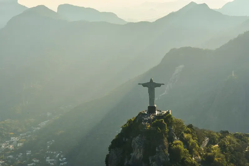 Estatua del Cristo Redentor sobre la cima de la montaña rodeada de neblina y paisaje montañoso.