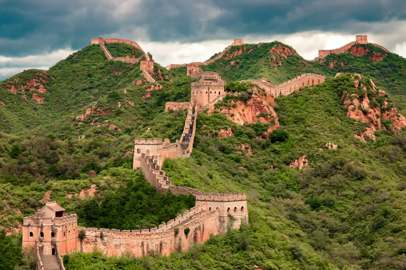 La Gran Muralla serpenteando sobre montañas verdes bajo un cielo nublado.