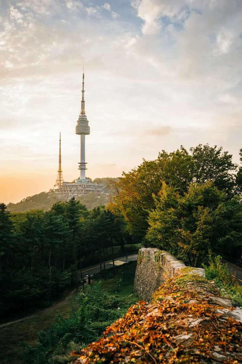 La Torre N Seoul en la cima de una colina arbolada vista desde una antigua muralla de piedra al atardecer.