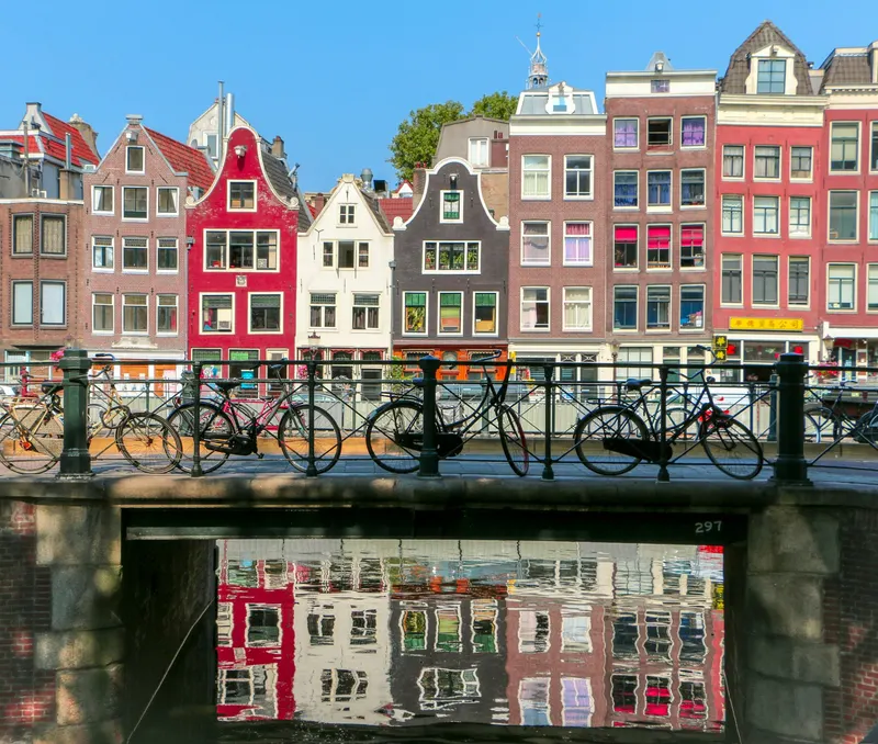 Casas coloridas de estilo tradicional junto a un canal en Ámsterdam con bicicletas estacionadas en un puente.