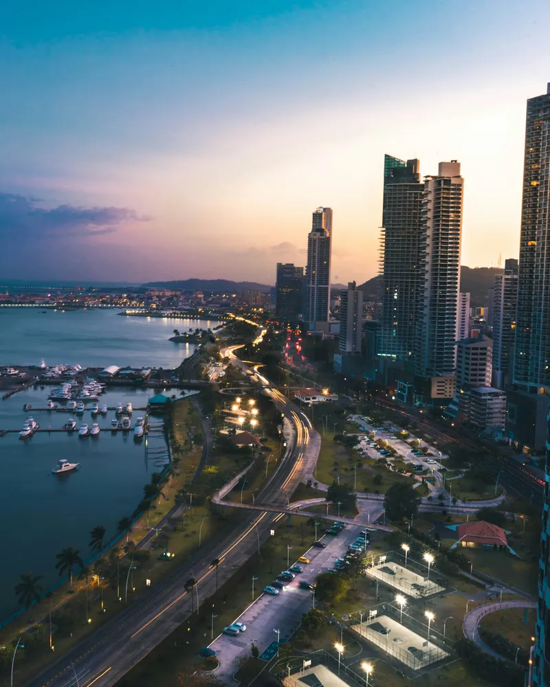 Rascacielos de la Ciudad de Panamá iluminados al atardecer frente a la bahía y una avenida costera con tráfico.