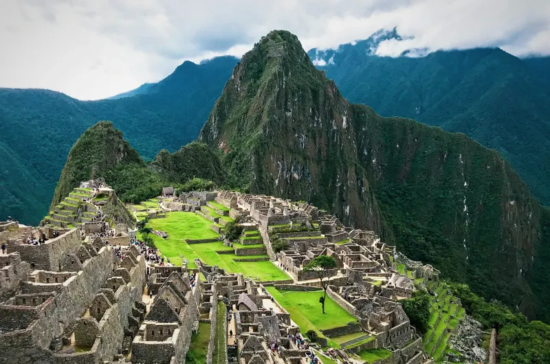 Ruinas de piedra de Machu Picchu sobre terrazas verdes rodeadas de altas montañas nubladas.