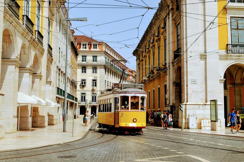 Tranvía amarillo número 25 transitando por una calle adoquinada con edificios clásicos blancos y amarillos en Lisboa.